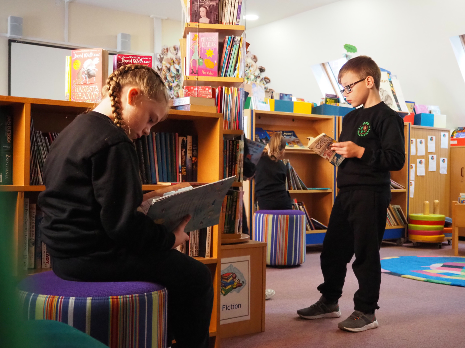 A girl and boy are seen browsing books together in the academy library.