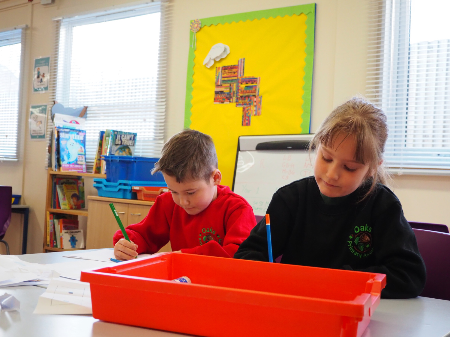 Two pupils are shown working together at a desk with pencils in their hands.