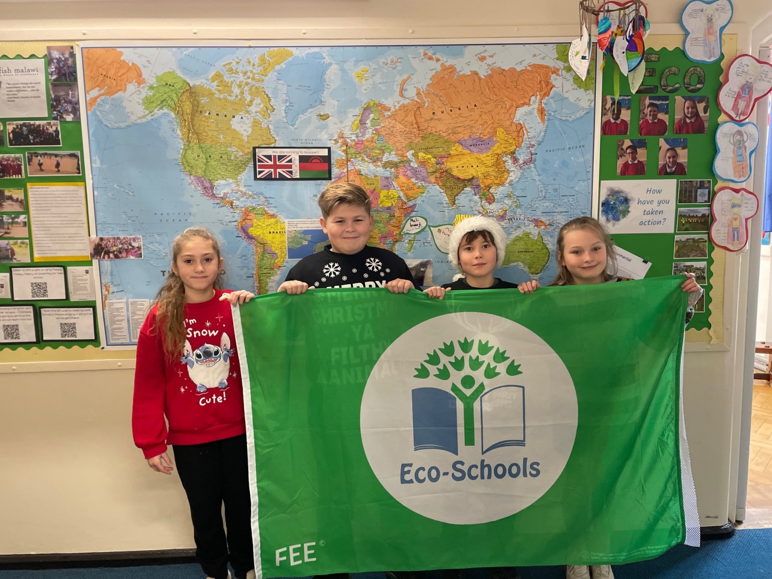 Four Oaks Primary Academy pupils are pictured smiling for the camera and holding up a banner with the Eco Schools logo on it.